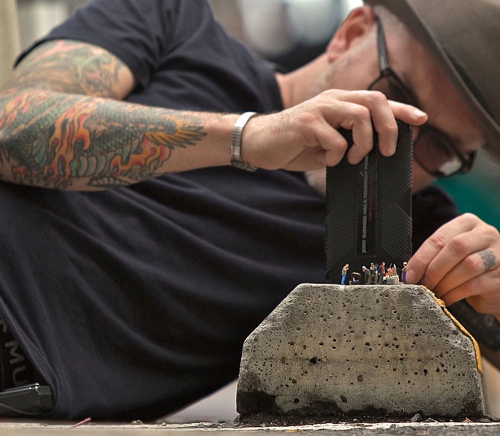 Jerry Business laying on his side using his iPhone of tiny figurine people placed on a rock